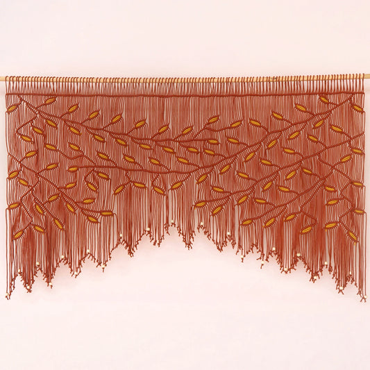 A brown fringed wall hanging or curtain with an embroidered leafy vine pattern, displayed against a plain light background.