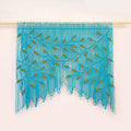 A turquoise blue fringed wall hanging or curtain with embroidered leaf-like details, suspended from a light wooden rod against a plain off-white wall.