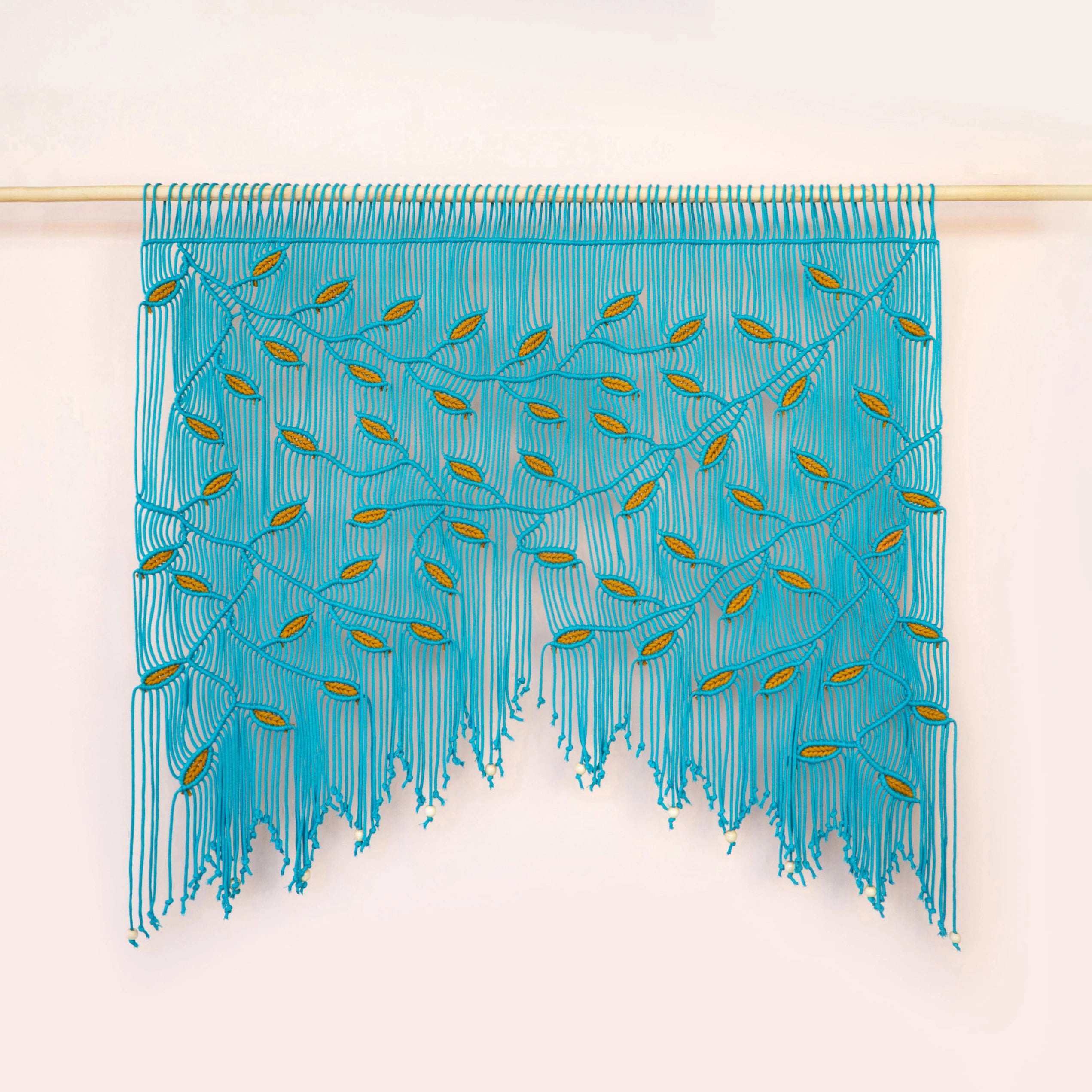 A turquoise blue fringed wall hanging or curtain with embroidered leaf-like details, suspended from a light wooden rod against a plain off-white wall.