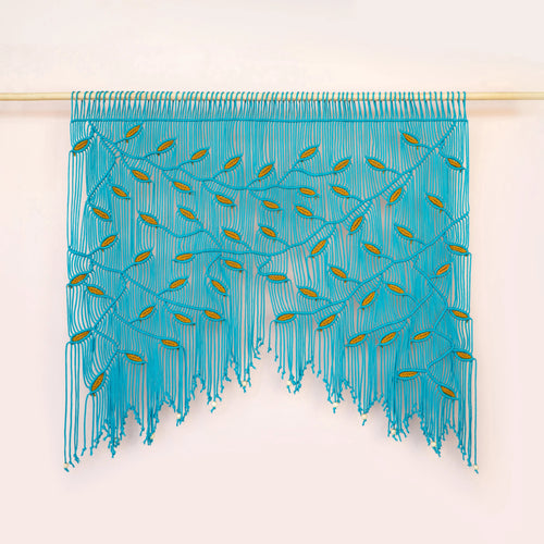A turquoise blue fringed wall hanging or curtain with embroidered leaf-like details, suspended from a light wooden rod against a plain off-white wall.
