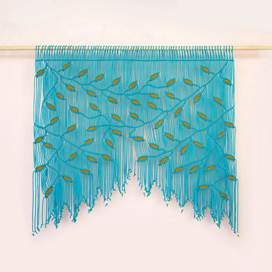 A turquoise blue fringed wall hanging or curtain with embroidered leaf-like details, suspended from a light wooden rod against a plain off-white wall.