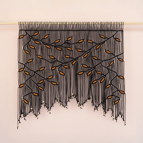Wide botanical macrame tapestry showcasing an arched branch canopy in dark black with warm ochre leaf highlights.