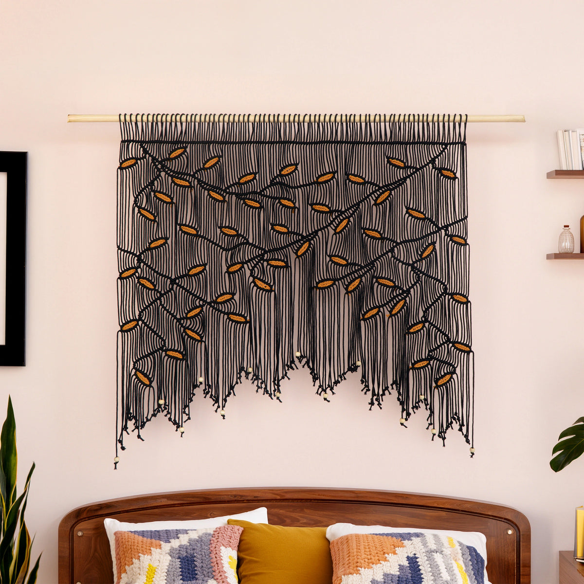 Large-scale black and mustard leaf fiber tapestry installed on a light wood rod against a warm neutral accent wall.