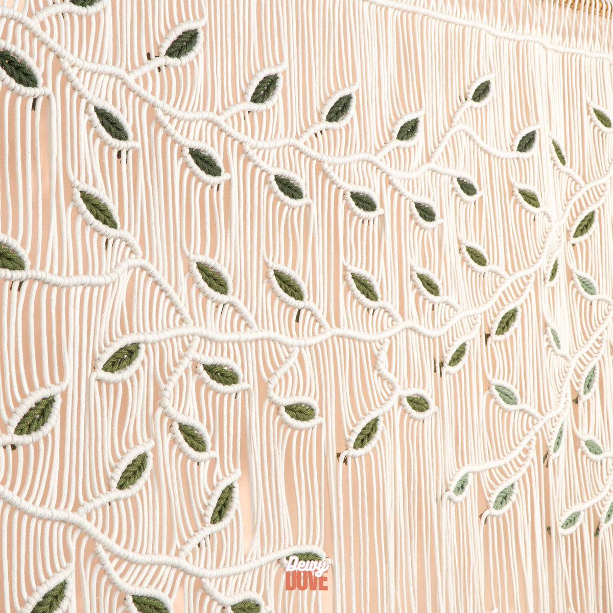 A close-up of a peach-colored textile with white embroidered leaf and vine patterns over vertical stitched lines.