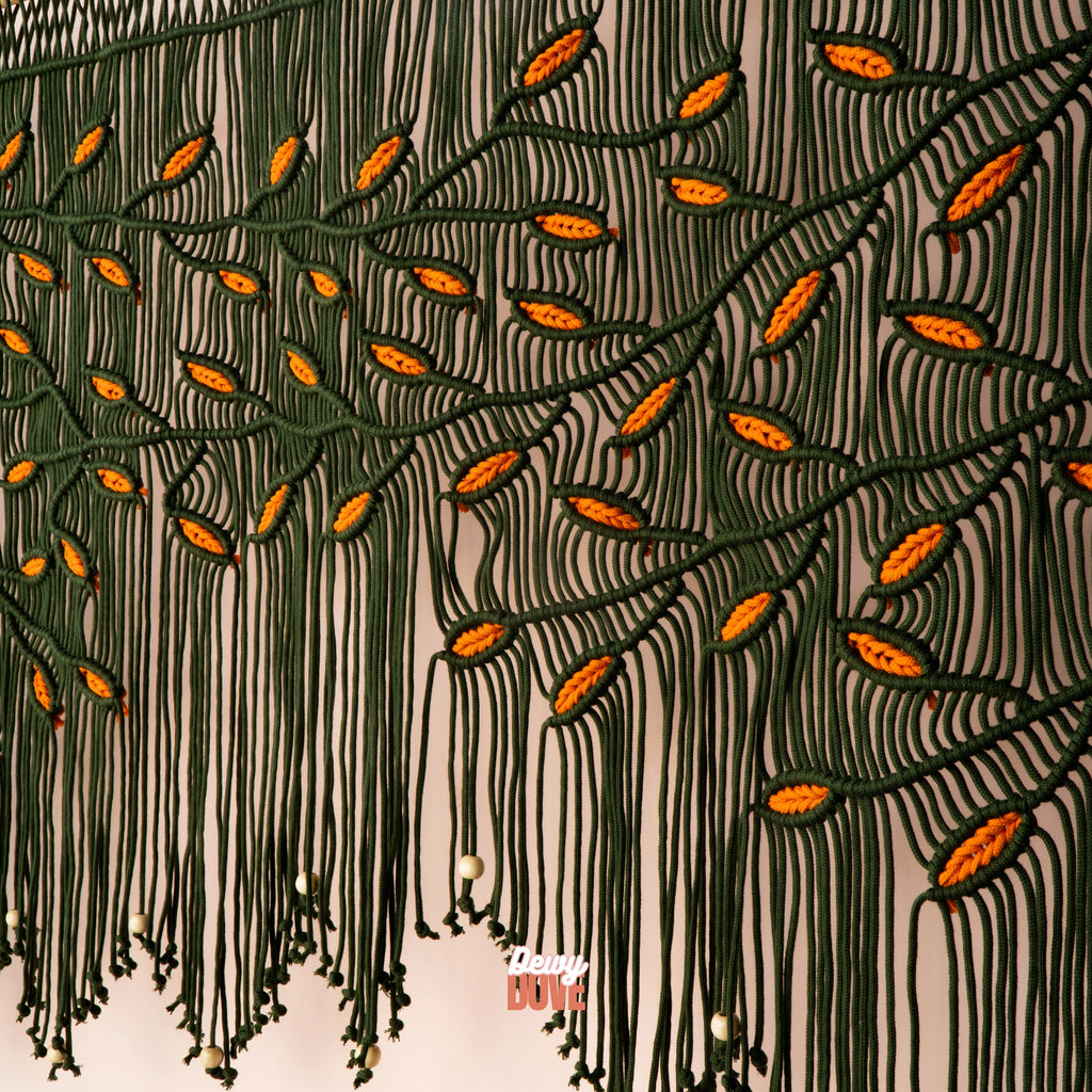 Hand-knotted botanical macrame backdrop displaying a cascading tree branch design with bright orange leaf accents and hanging wooden beads.