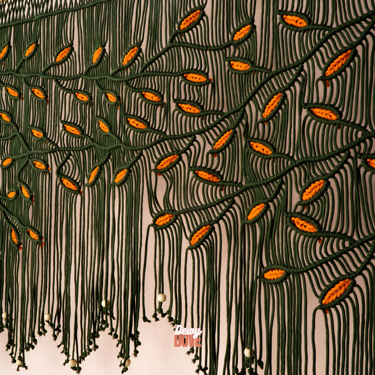 Hand-knotted botanical macrame backdrop displaying a cascading tree branch design with bright orange leaf accents and hanging wooden beads.