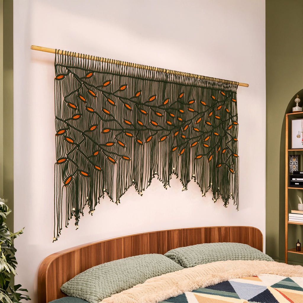 Earth-toned macrame wall hanging in rich dark green with contrasting orange leaf details, perfectly styled for eclectic and autumn-inspired living spaces.