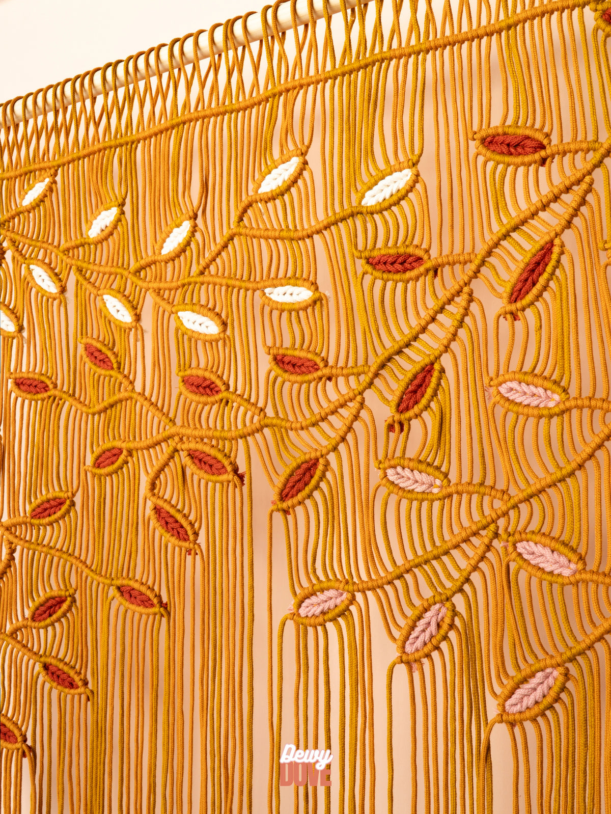A close-up of a beige curtain featuring intricate golden-yellow rope embroidery in a leafy vine pattern, accented with small white, pink, and rust-colored details.