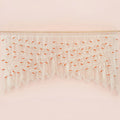 Handcrafted natural beige macrame wall hanging featuring an intricate botanical canopy of cream cords and vibrant orange leaves, hung above a rust-colored velvet sofa.