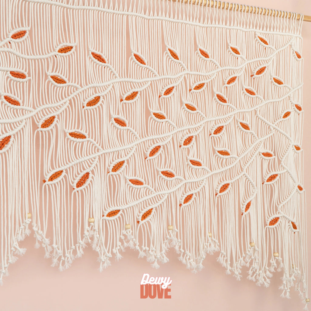 Oversized natural macrame tapestry with scalloped fringe and wooden beads, displaying a symmetrical weeping tree branch pattern and bright orange leaf accents.