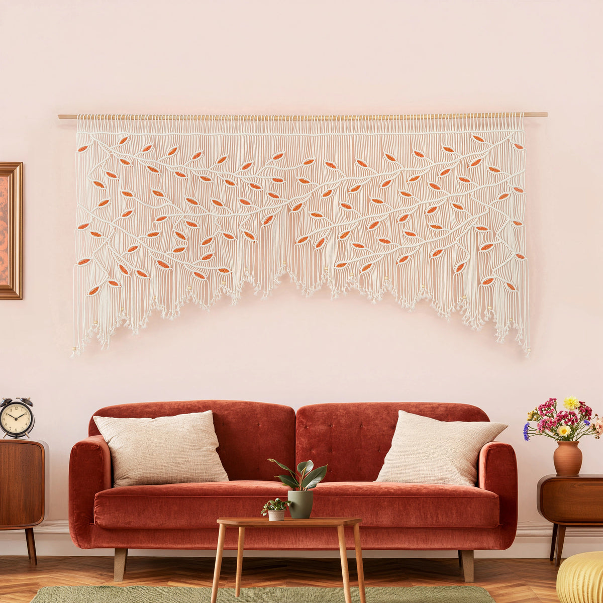 Large natural and orange leaf macrame wall art hanging horizontally on a smooth wooden dowel against a soft pinkish-neutral interior wall.