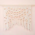 Handcrafted natural beige macrame wall hanging featuring an intricate botanical canopy of cream-colored vines and vibrant orange leaves.