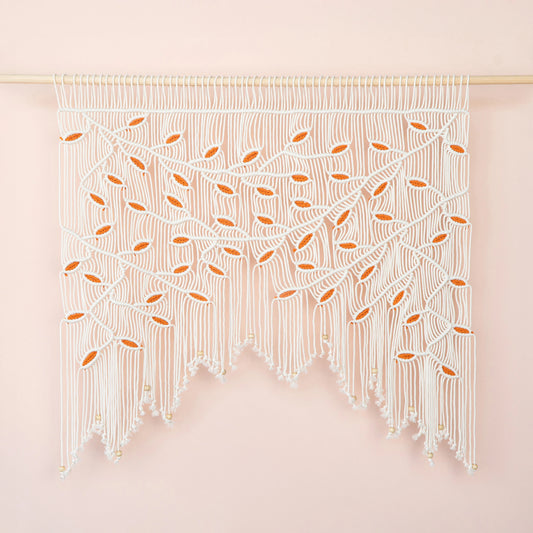 Handcrafted natural beige macrame wall hanging featuring an intricate botanical canopy of cream-colored vines and vibrant orange leaves.