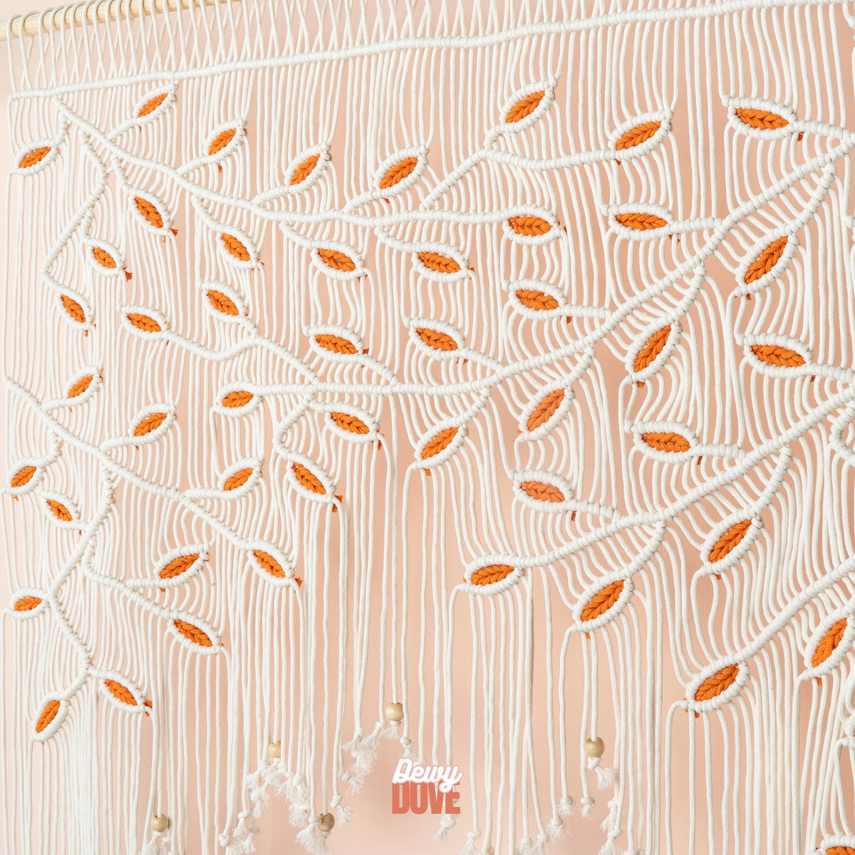 Large natural beige and orange leaf macrame wall art hanging horizontally on a smooth wooden dowel above a modern bedroom headboard.