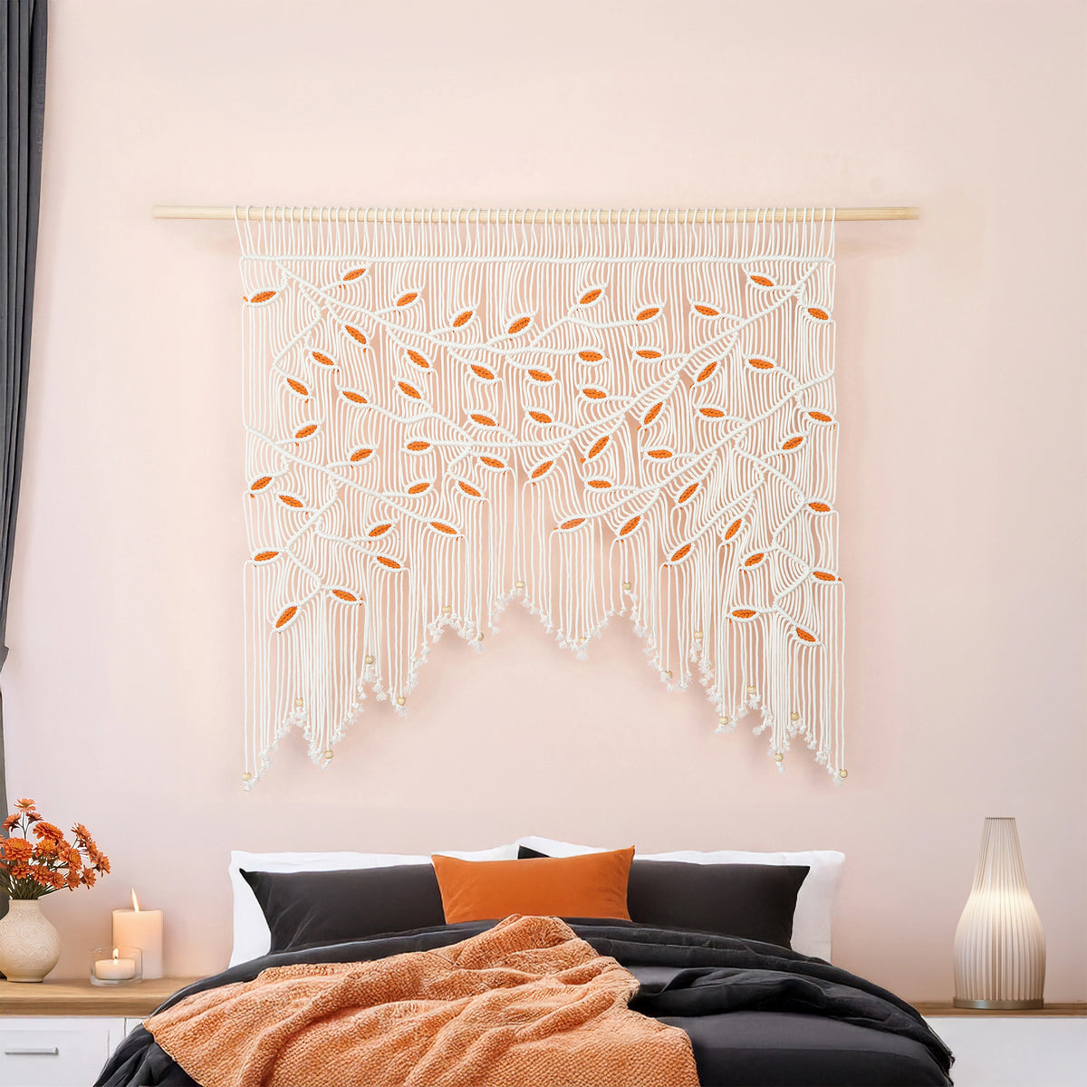 Detailed close-up of a creamy natural macrame wall hanging showing precise knotwork and contrasting vibrant orange botanical leaf motifs.