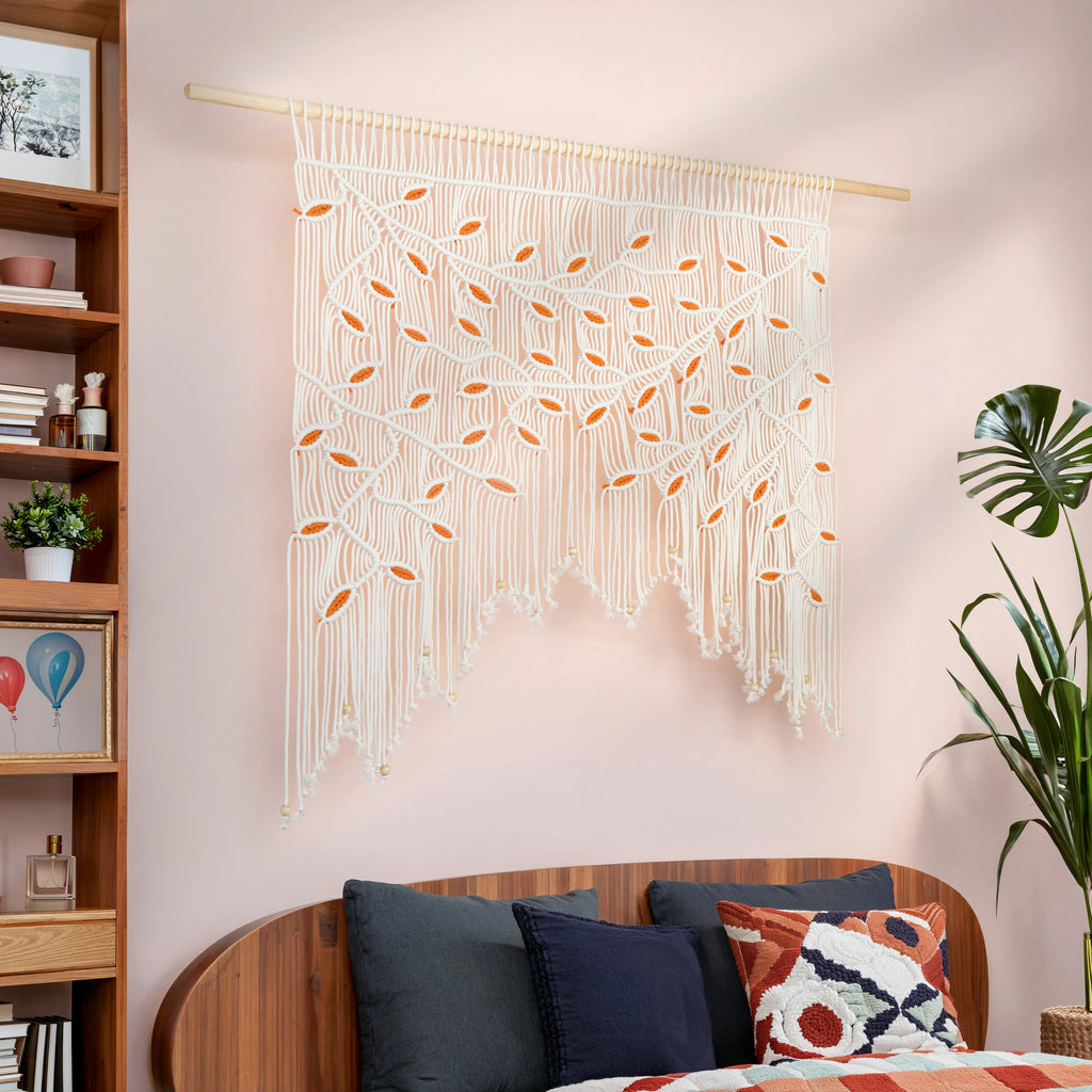 Wide botanical macrame tapestry showcasing an arched branch canopy in soft cream with warm orange leaf highlights.