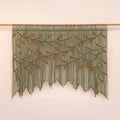 Handcrafted olive green macrame wall hanging featuring an intricate botanical canopy of deep green vines and vibrant orange leaves.
