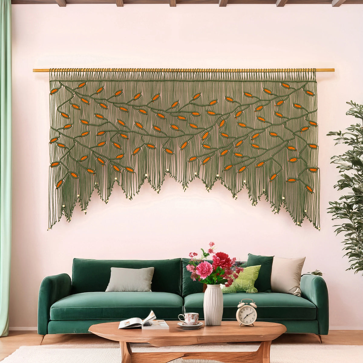Detailed close-up of a rich olive green macrame wall hanging showing precise knotwork and contrasting vibrant orange botanical leaf motifs over a green seating area.