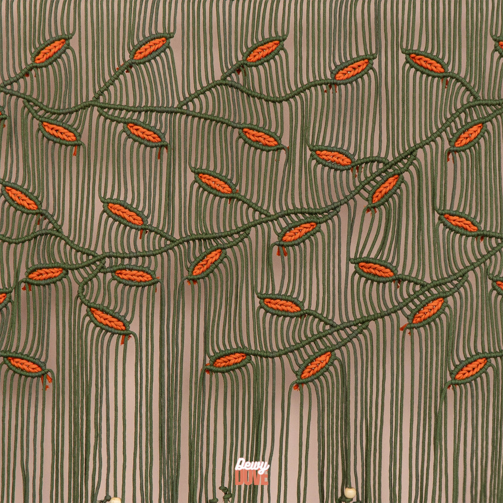 Large olive green and orange leaf macrame wall art hanging horizontally on a smooth wooden dowel above a modern wooden console table.