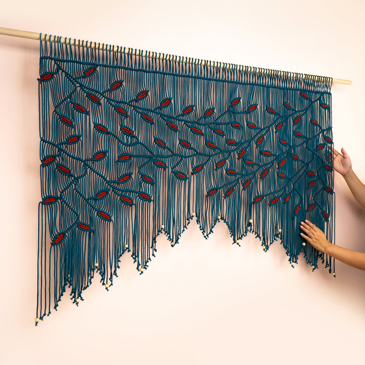 Black and orange woven wall art with a person's hands holding it against a light pink background