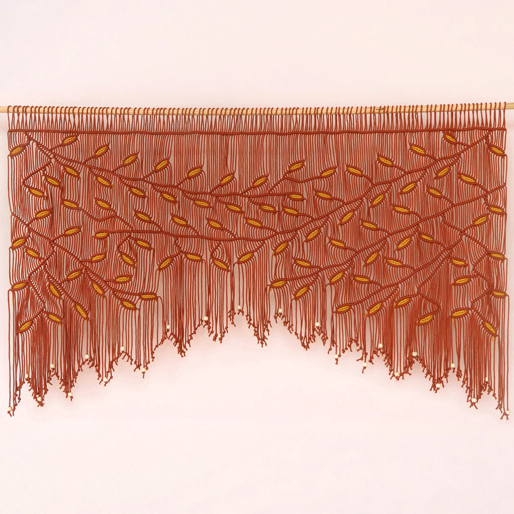 A brown fringed wall hanging or curtain with an embroidered leafy vine pattern, displayed against a plain light background.