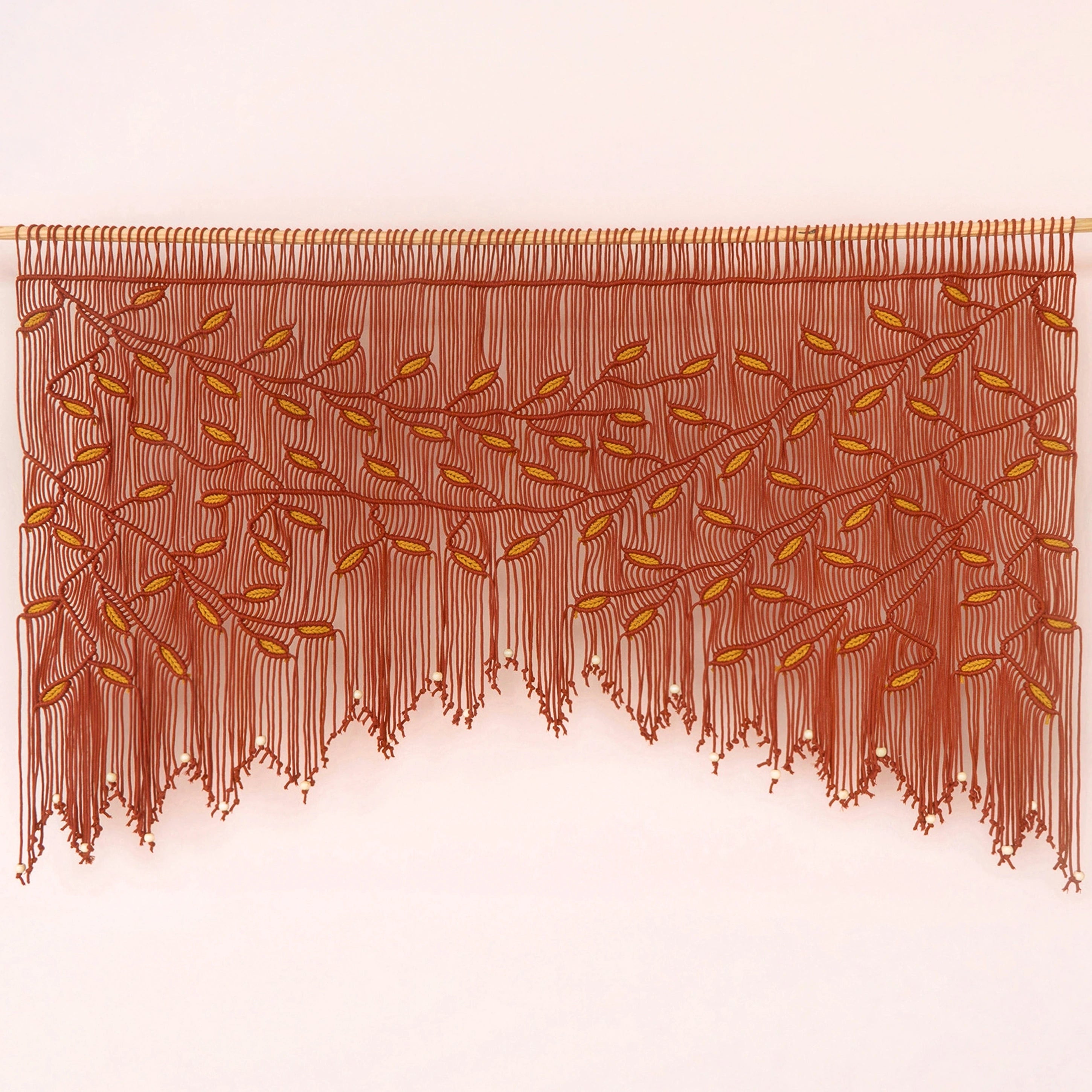A brown fringed wall hanging or curtain with an embroidered leafy vine pattern, displayed against a plain light background.