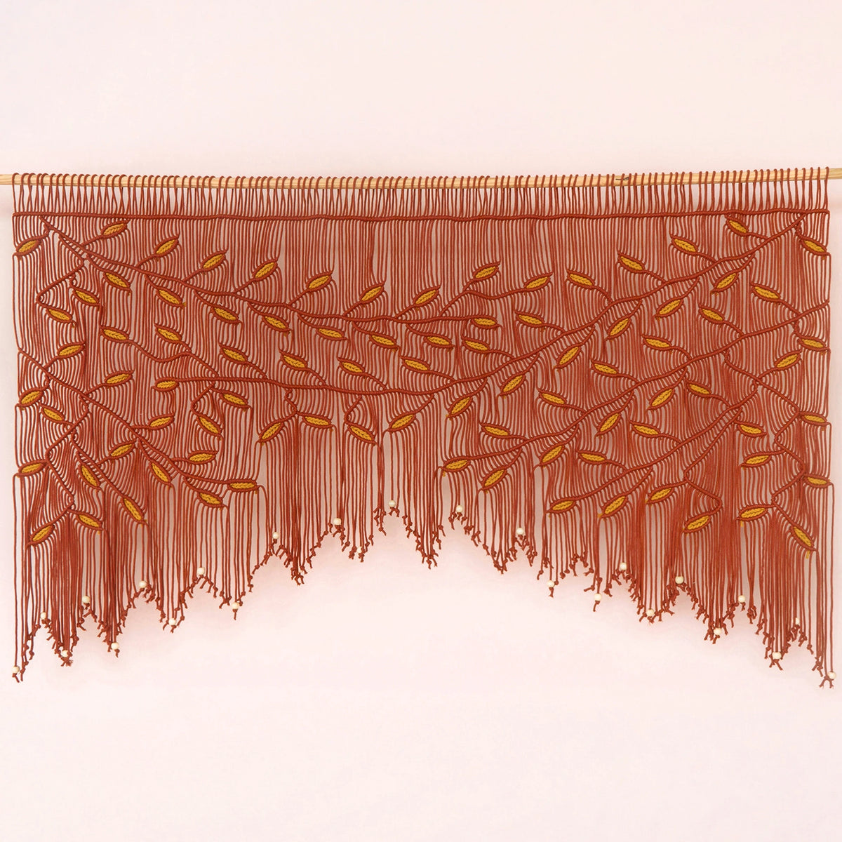A brown fringed wall hanging or curtain with an embroidered leafy vine pattern, displayed against a plain light background.